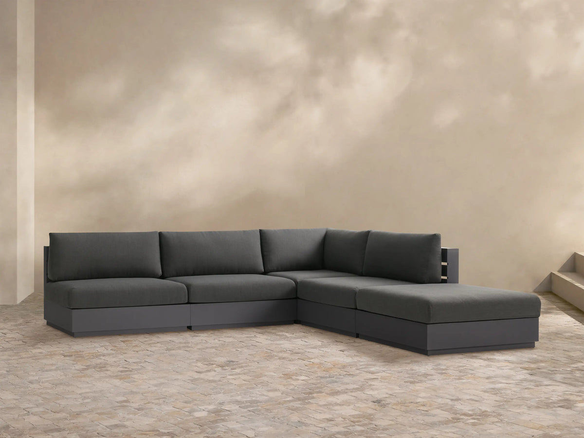 Bal Harbour Outdoor Aluminum L-shaped sectional in dark gray fabric, with a charcoal base, on a light stone patio.