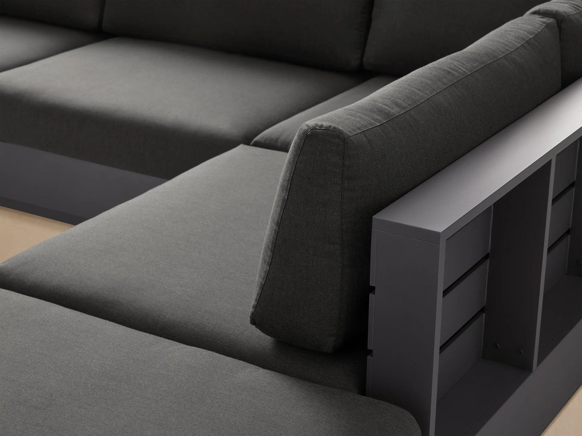 Bal Harbour five-piece L-shaped dark gray aluminum outdoor sectional sofa with ottoman on a light patio, against a beige wall.