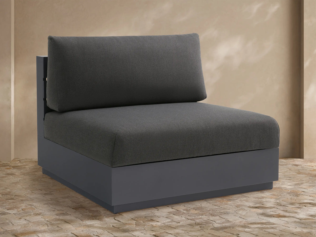 Bal Harbour Outdoor Armless Chair with charcoal fabric cushions on a dark gray aluminum base, set against a warm-toned outdoor wall.