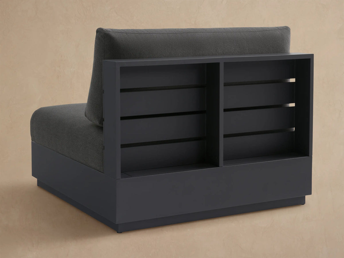 Dark gray Bal Harbour Outdoor Aluminum Armless Chair, upholstered cushions, slatted frame, shown from an angle.