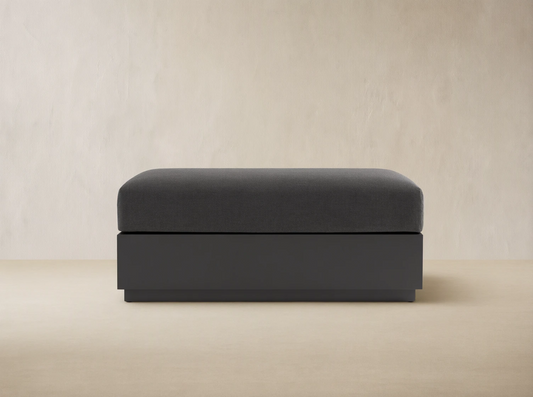 Bal Harbour Outdoor Aluminum Ottoman with a dark gray fabric cushion and a matte dark gray aluminum base on a stone floor.