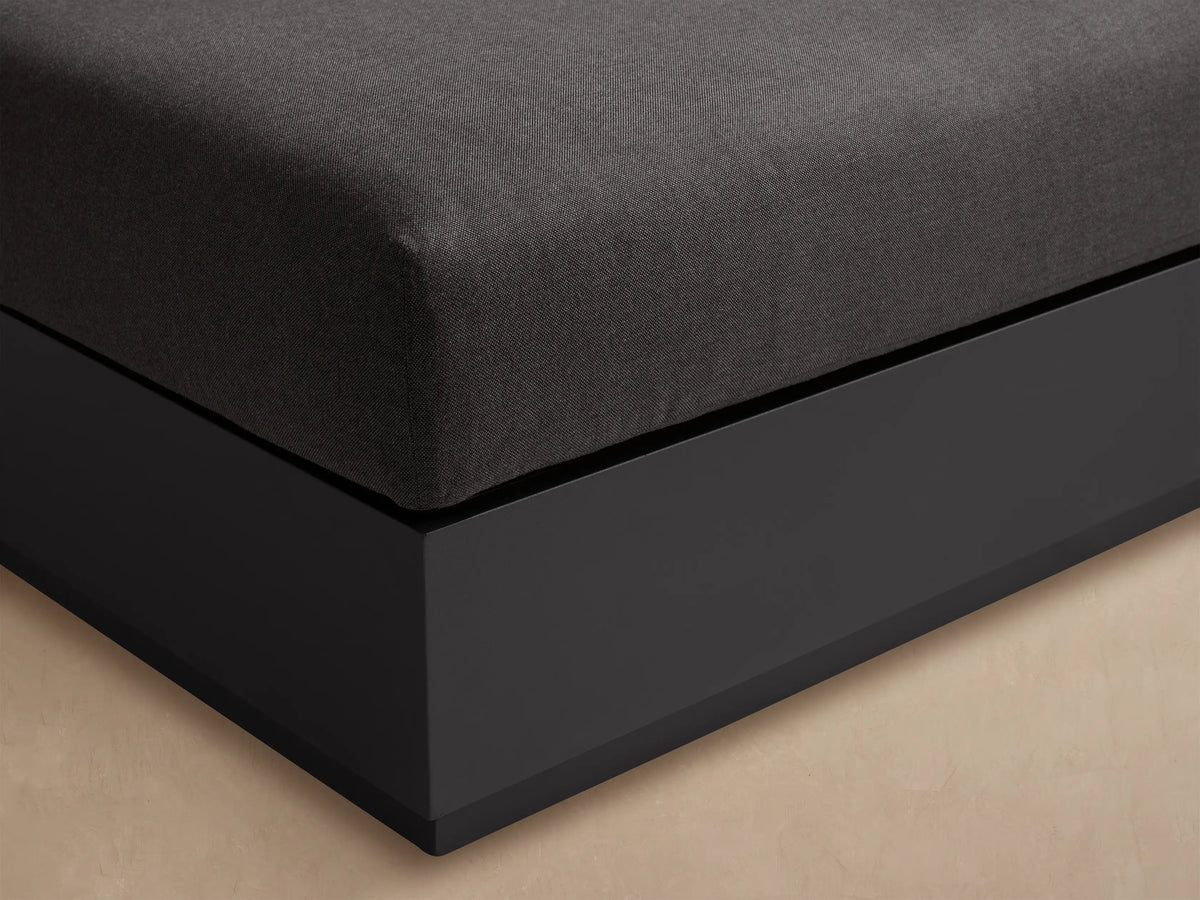 Bal Harbour Outdoor Aluminum Ottoman. Square, dark gray cushion on a sleek charcoal aluminum frame, set on a textured patio.