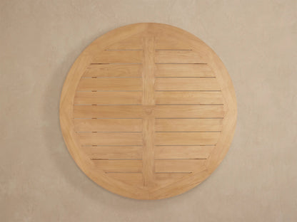 Close-up of Bal Harbour Outdoor Teak Round Dining Table; light golden-brown slatted top, natural wood grain, curved edge, sturdy leg.