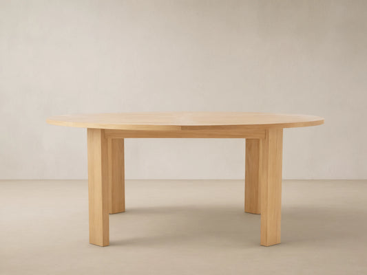 Round Bal Harbour outdoor dining table, light golden teak wood, with a slatted top and thick, sturdy legs on a tiled patio.