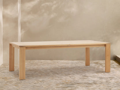 Bal Harbour Outdoor Teak Extension Dining Table, light natural wood, rectangular with slatted top, against a beige wall & stone floor.