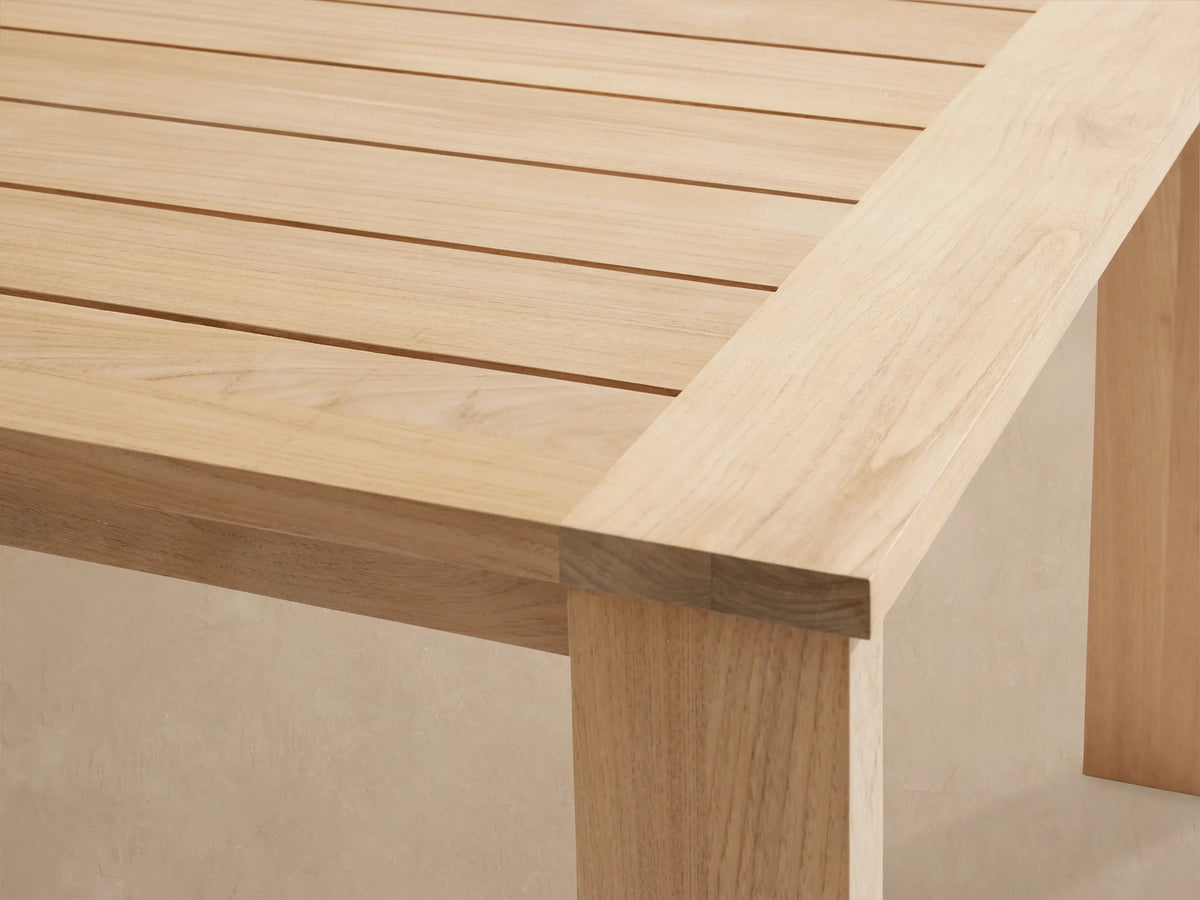 Bal Harbour Outdoor Teak Extension Dining Table, light natural wood with slatted top & thick square legs, on a patio.