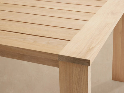 Bal Harbour Outdoor Teak Extension Dining Table, light natural wood with slatted top & thick square legs, on a patio.