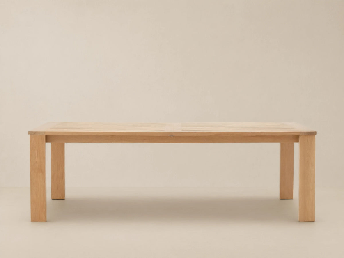 Bal Harbour Outdoor Teak Extension Dining Table, light teak wood with slatted top and sturdy legs, on a stone patio.