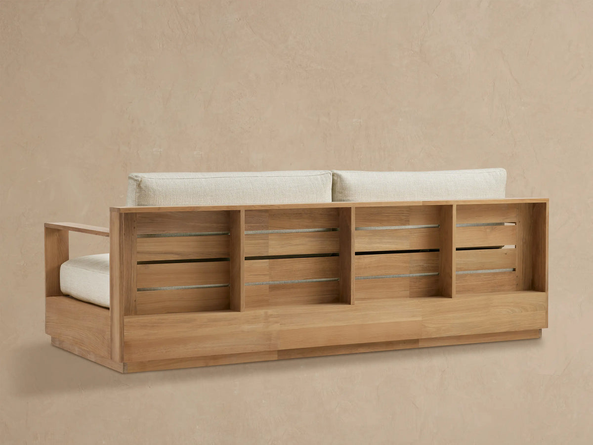 Close-up of Bal Harbour Outdoor Teak Sofa's natural teak wood right armrest and textured cream seat cushion.