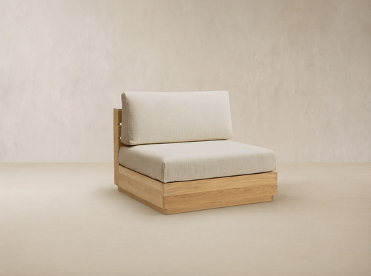 Bal Harbour Outdoor Teak Armless Chair with light natural wood base, light beige seat & back cushions, on a stone patio.