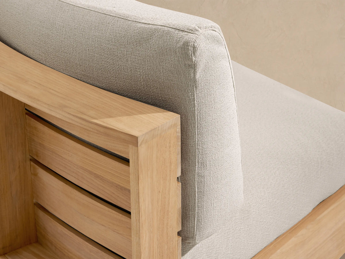 Bal Harbour Outdoor Curved Sofa with light beige cushions and natural teak wood curved base, on a stone tile floor.