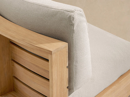 Bal Harbour Outdoor Curved Sofa with light beige cushions and natural teak wood curved base, on a stone tile floor.