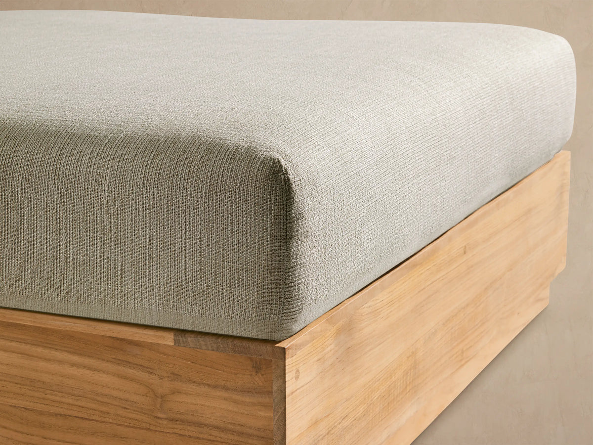 Bal Harbour Outdoor Teak Ottoman. Light cream cushioned, natural teak wood base, squared, on an outdoor patio.