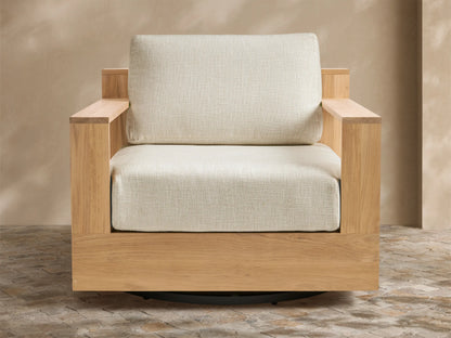 Bal Harbour Outdoor Teak Swivel Chair, golden teak frame, light beige cushions, black swivel base, angled on a patio.