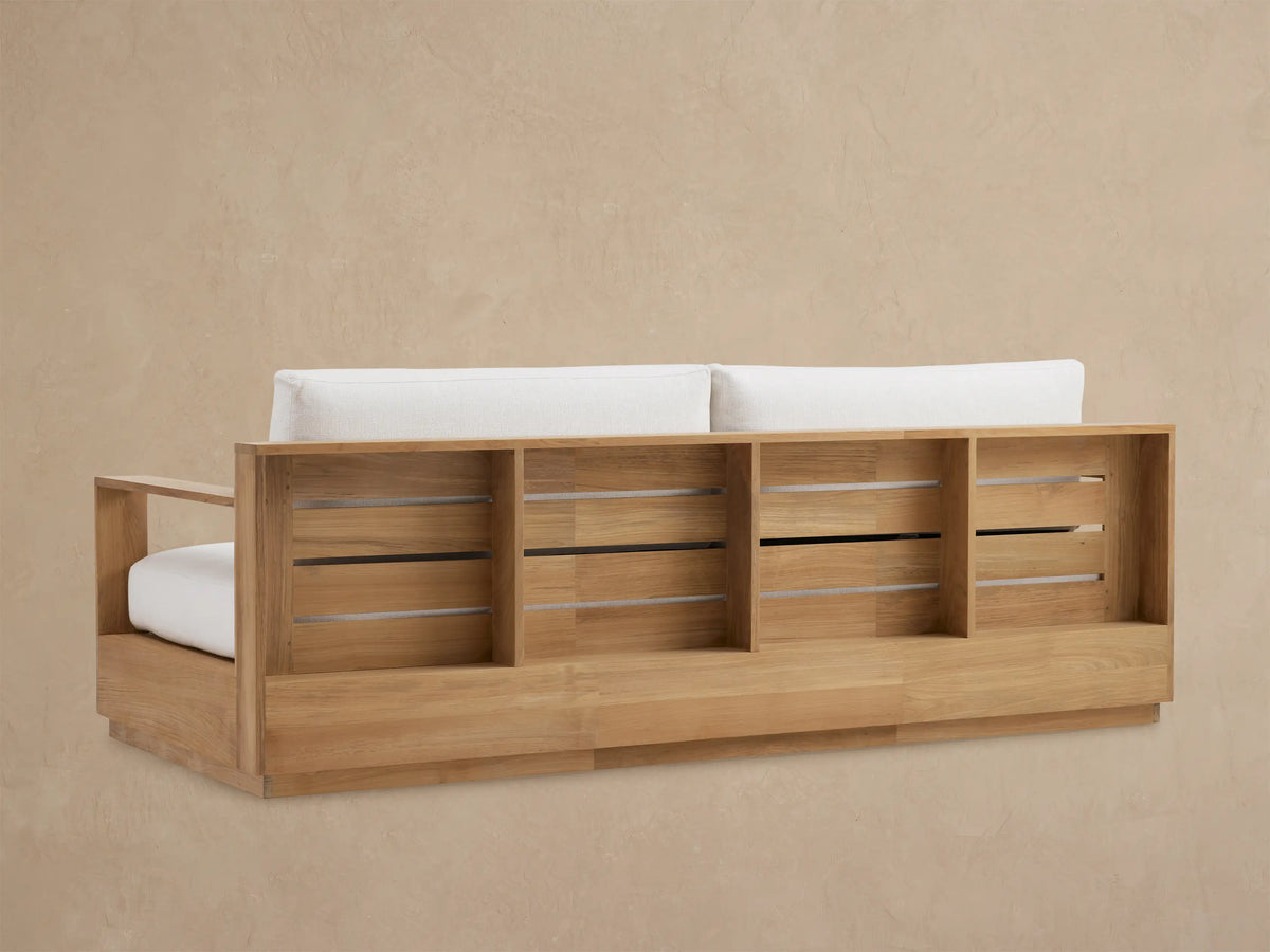 Close-up of Bal Harbour Outdoor Teak Sofa, showing natural teak wood armrest and frame with thick white cushions.
