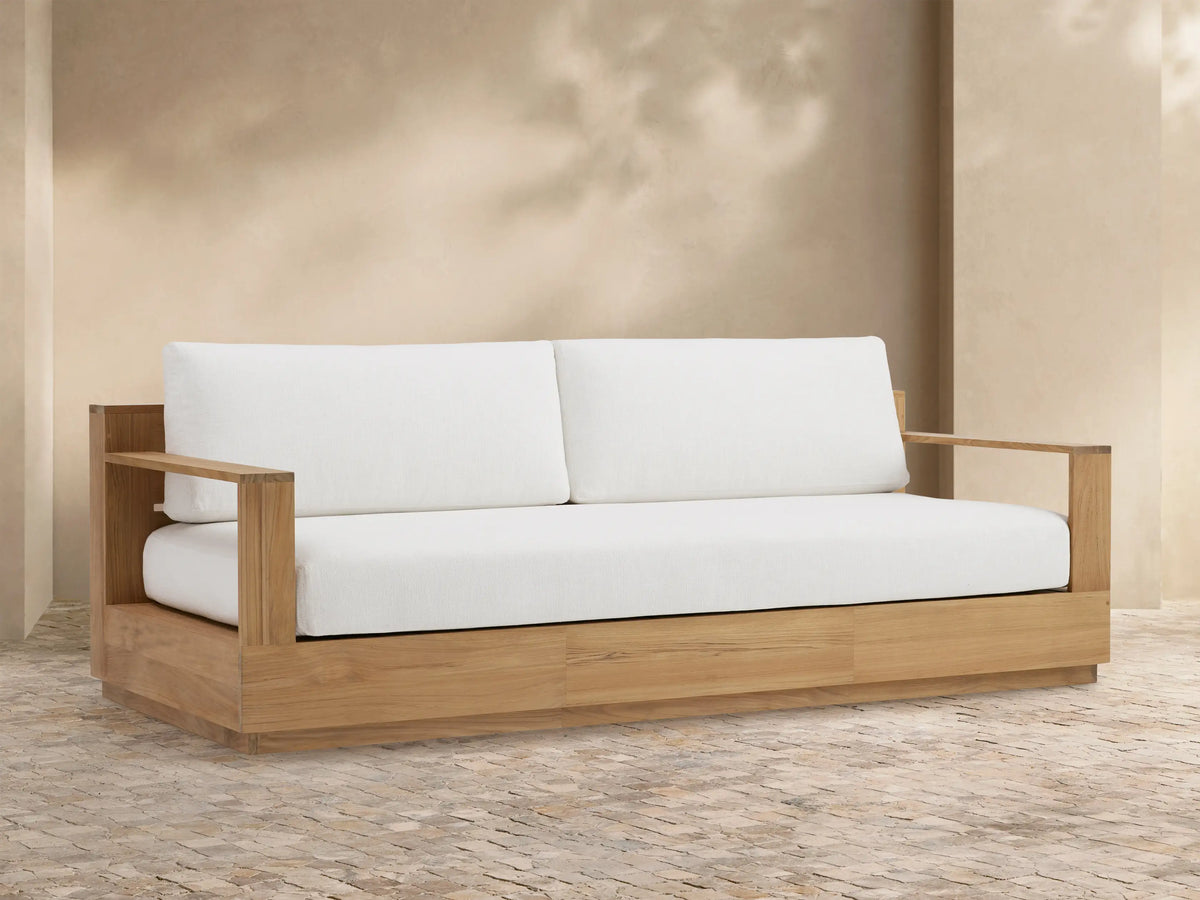 Bal Harbour Outdoor Teak Sofa, natural teak wood frame with two white back cushions and one white seat cushion, on a patio.