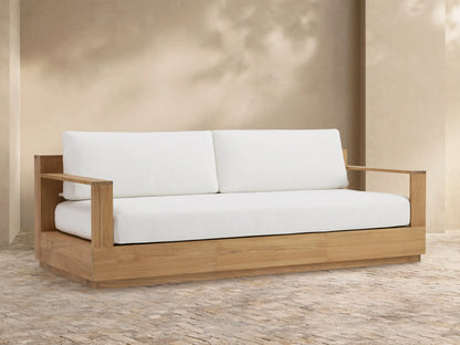 Bal Harbour Outdoor Teak Sofa, natural teak wood frame with two white back cushions and one white seat cushion, on a patio.