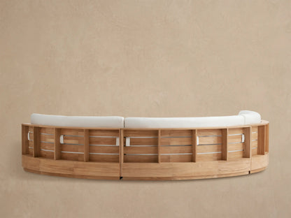 Close-up of Bal Harbour Outdoor Curved Sectional back. Light wood frame with curved slats supports a thick, light beige cushion.