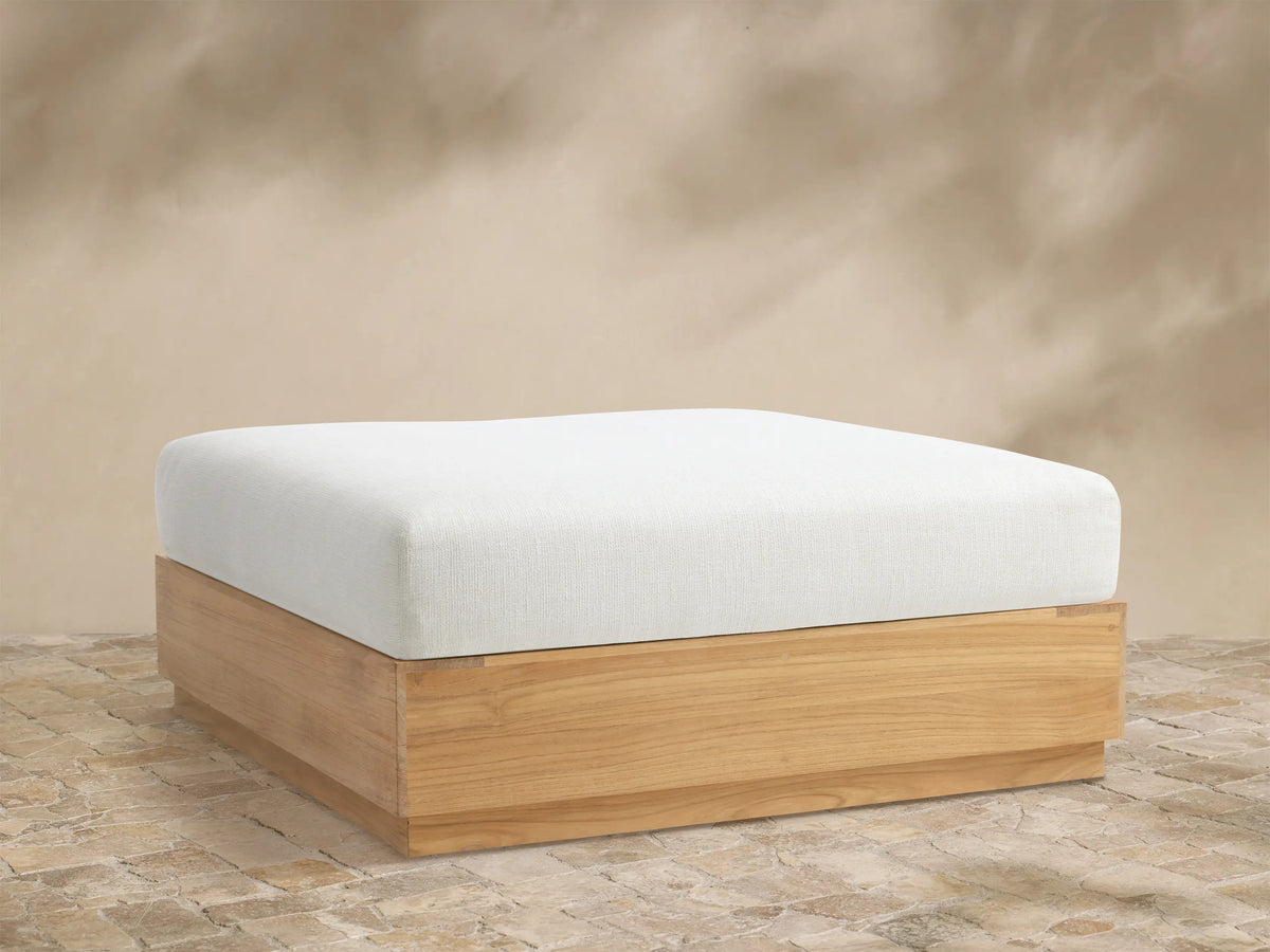 Bal Harbour Outdoor Teak Ottoman, front view. White cushion sits on a natural light brown teak wood base on a tiled floor.