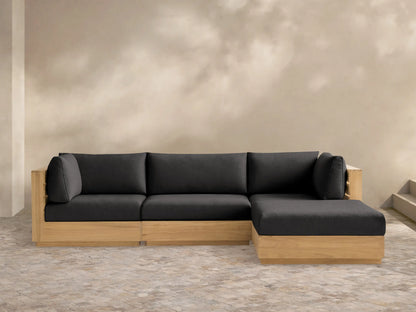 Bal Harbour Four-Piece Teak Sectional: L-shaped light wood frame, dark gray cushions, against light wall on tiled floor.