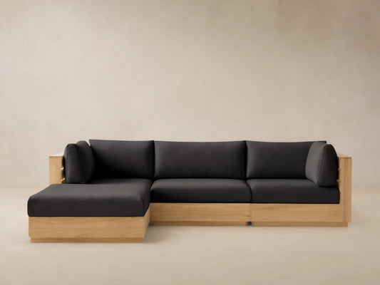 Bal Harbour Four-Piece Teak Sectional: L-shaped light wood frame, dark gray cushions, against light wall on tiled floor.