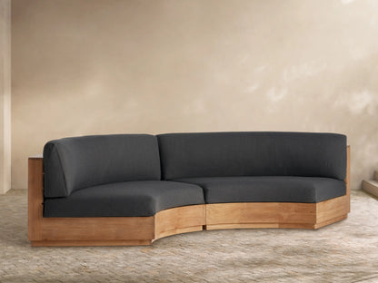Bal Harbour Outdoor Curved Two-Piece Sectional with natural teak base and charcoal cushions on a paved outdoor patio.