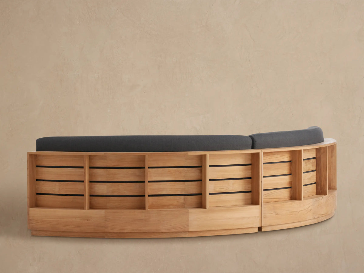 Close-up of Bal Harbour Outdoor Sectional's curved dark gray back cushion on a light brown slatted teak wood frame.