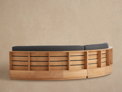 Close-up of Bal Harbour Outdoor Sectional's curved dark gray back cushion on a light brown slatted teak wood frame.