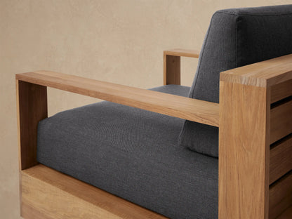 Golden teak Bal Harbour Outdoor Teak Swivel Chair, front view, with thick dark gray seat and back cushions on a patio.