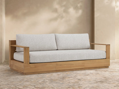 Bal Harbour Outdoor Teak Sofa with light golden-brown wood frame, light grey cushions, centered against a beige wall.