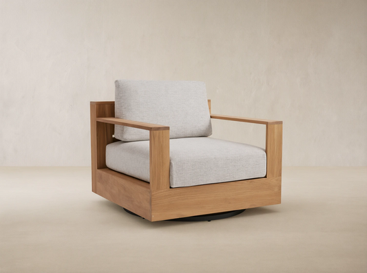 Bal Harbour Outdoor Teak Swivel Chair with natural golden-brown teak frame, light gray cushions, and black swivel base on a patio.