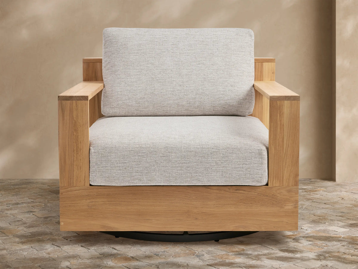 Bal Harbour Outdoor Teak Swivel Chair with natural golden-brown teak frame, light gray cushions, and black swivel base on a patio.
