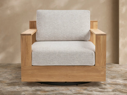 Bal Harbour Outdoor Teak Swivel Chair with natural golden-brown teak frame, light gray cushions, and black swivel base on a patio.