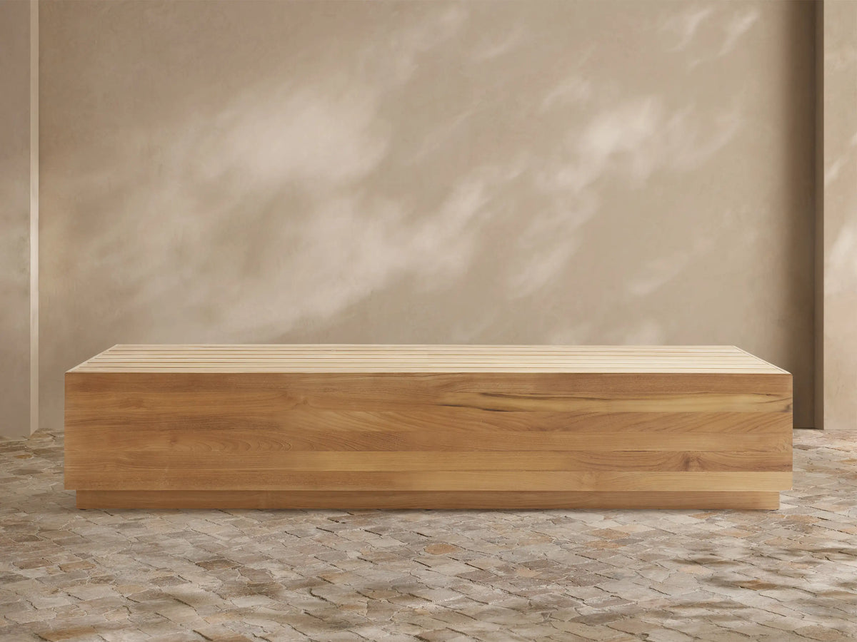 Bal Harbour Outdoor Teak Coffee Table: Rectangular light golden-brown teak table with slatted top on a stone floor, natural light.