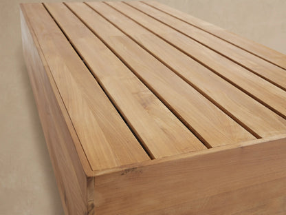 Low rectangular Bal Harbour Outdoor Teak Coffee Table, natural golden wood with slatted top, on stone pavers.