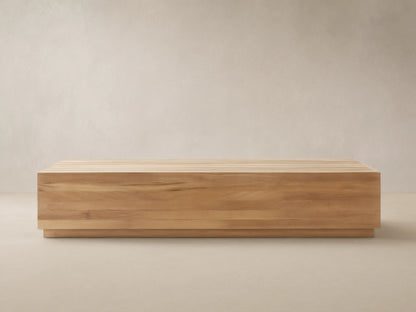 Bal Harbour Outdoor Teak Coffee Table: Rectangular light golden-brown teak table with slatted top on a stone floor, natural light.