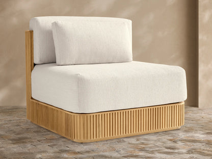 Beaumont Teak Lounge Chair. Front view of modern chair with slatted natural teak base & thick cream cushions on a stone patio.