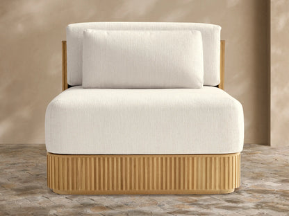 Beaumont Teak Lounge Chair. Front view of modern chair with slatted natural teak base & thick cream cushions on a stone patio.