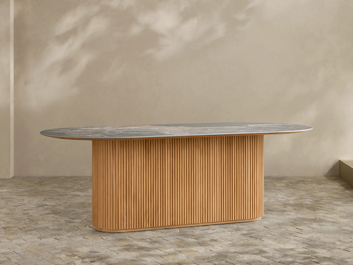 Beaumont Outdoor Teak Dining Table with oval dark gray sintered stone top on a golden slatted teak wood base.