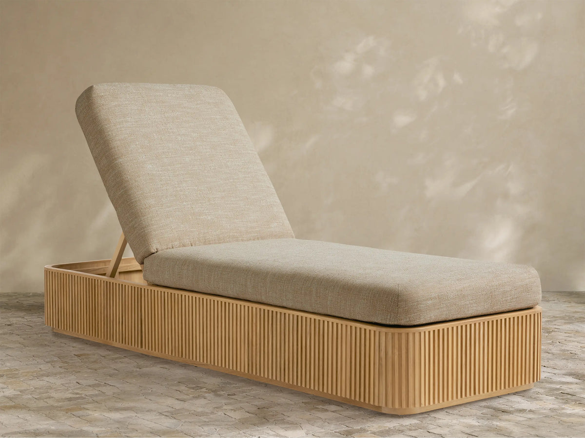 Beaumont Outdoor Teak Chaise with light beige cushions, angled backrest, and slatted teak wood base on a patterned floor.