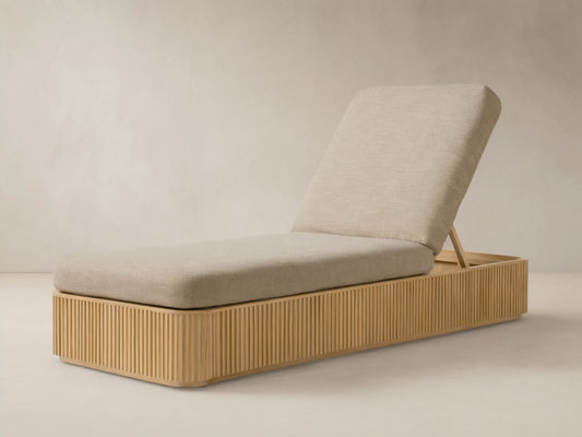 Beaumont Outdoor Teak Chaise with light beige cushions, angled backrest, and slatted teak wood base on a patterned floor.