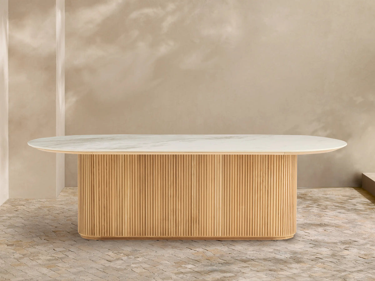 Beaumont Outdoor Teak Dining Table: Oval white marbled top on a natural golden fluted teak wood pedestal base, outdoor patio.