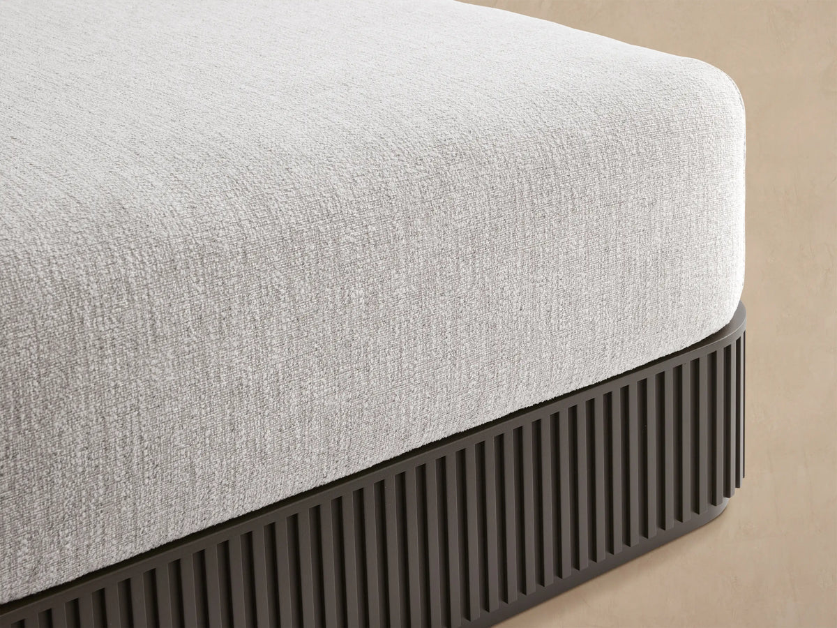 Beaumont Outdoor Aluminum Ottoman, light gray cushion on dark gray ribbed aluminum base, on a stone patio.