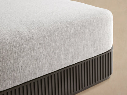 Beaumont Outdoor Aluminum Ottoman, light gray cushion on dark gray ribbed aluminum base, on a stone patio.