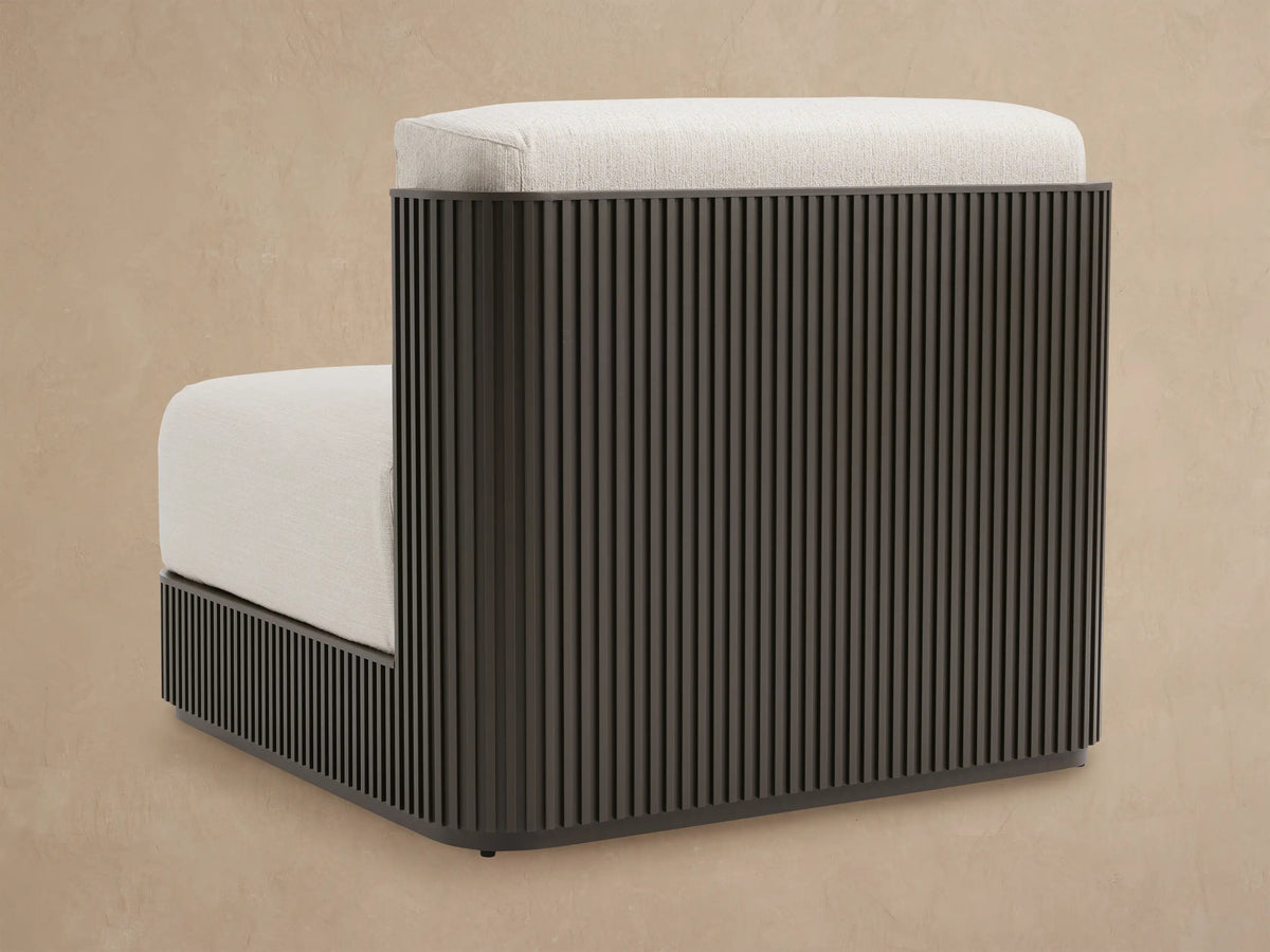 Close-up of Beaumont Outdoor Aluminum Lounge Chair, dark slatted frame, rounded armrest, and light textured cushions.