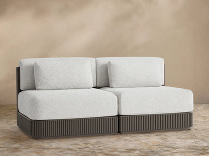 Beaumont Outdoor Aluminum Two-Piece Modular Sofa with light grey cushions and dark brown slatted bases, against a tan wall.