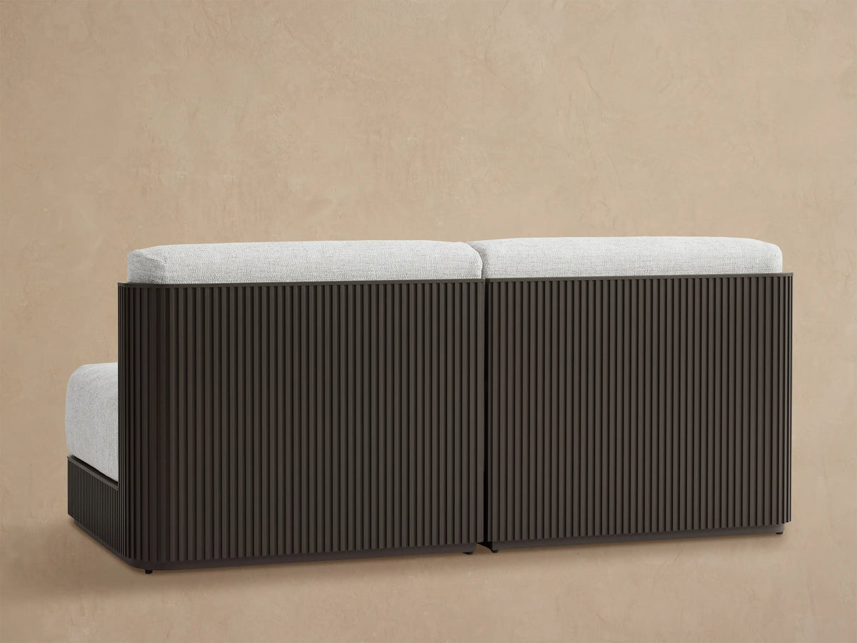 Close-up of Beaumont Modular Sofa corner with light grey textured cushions & dark slatted aluminum frame against a beige wall.