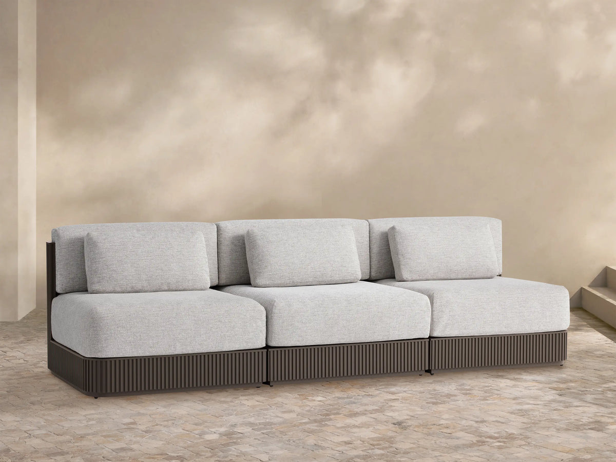 Beaumont Outdoor Aluminum Three-Piece Modular Sofa in light gray with a dark brown slatted aluminum base on a tiled patio.