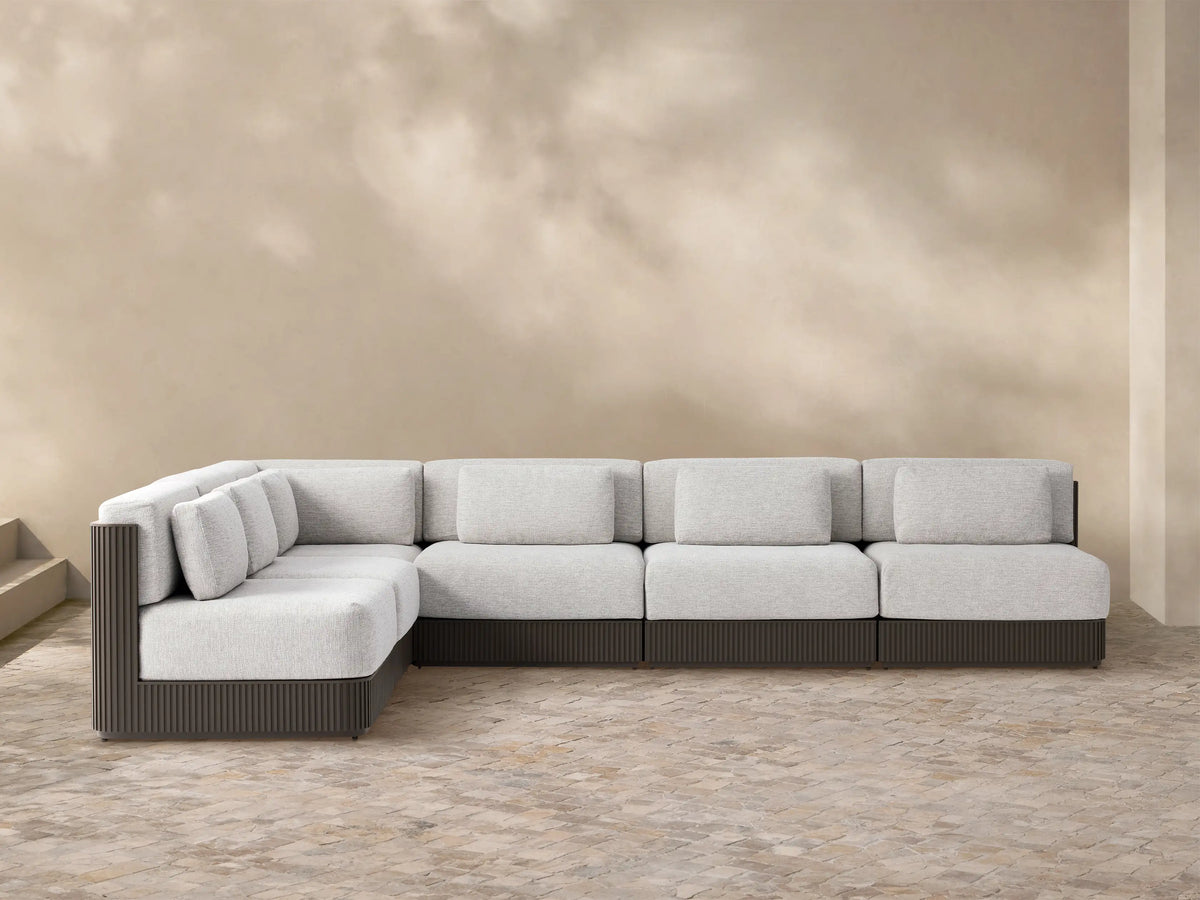 L-shaped Beaumont Outdoor Aluminum Six-Piece Sectional with light grey cushions & dark ribbed aluminum frame on patio stones.