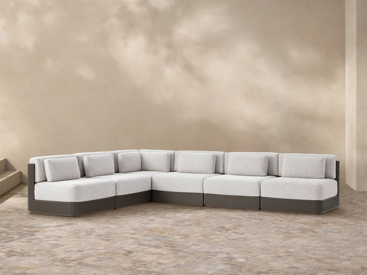 L-shaped Beaumont Outdoor Aluminum Six-Piece Sectional with light grey cushions & dark ribbed aluminum frame on patio stones.